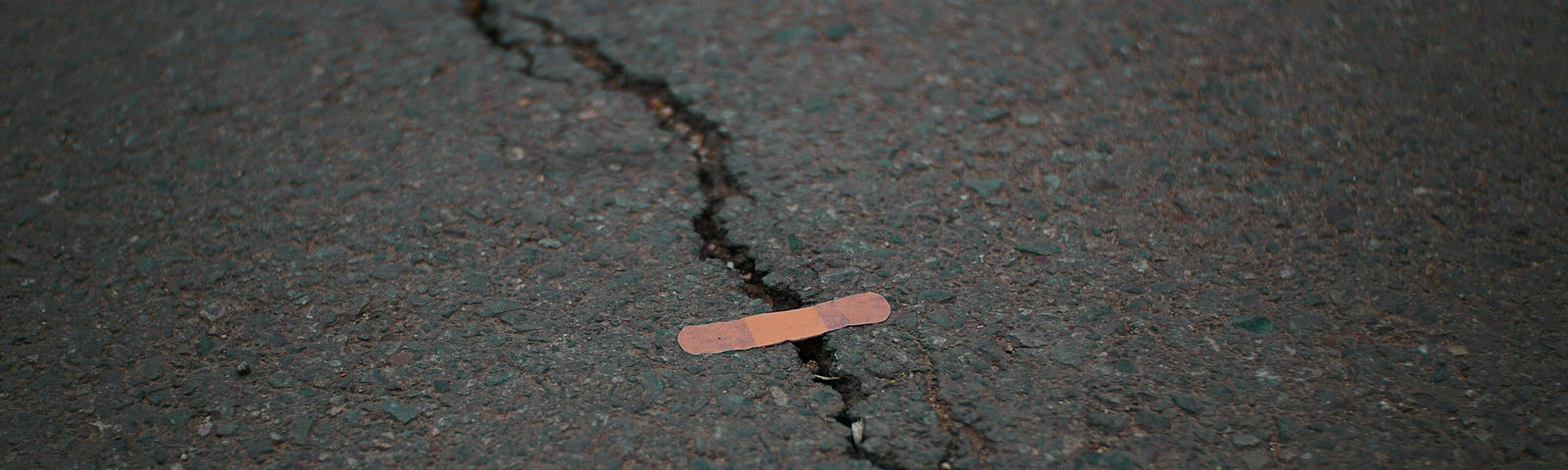 A jagged crack in the road with a Band Aid crossing it.