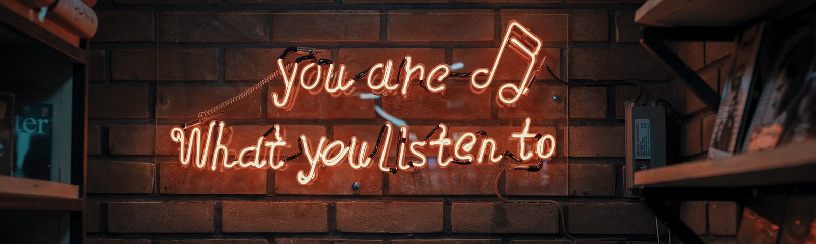 photo of text ‘you are what you listen to’ in neon lights aside music notes hanging in brick wall. Photo on Dr. James Goydos 2021 article on physician satisfaction podcasts