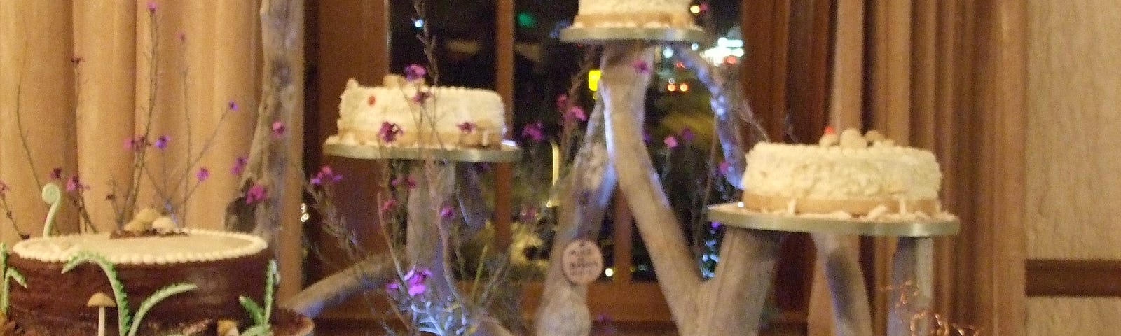 A softly lit table holding 5 birthday cakes on separate tiers.