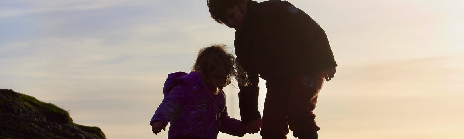 Two children are holding hands climbing down a rocky precipice