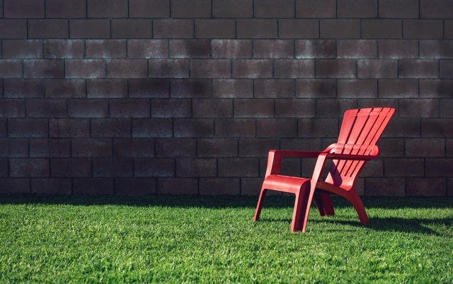 Plastic red chair sitting empty on glass with brick wall backdrop