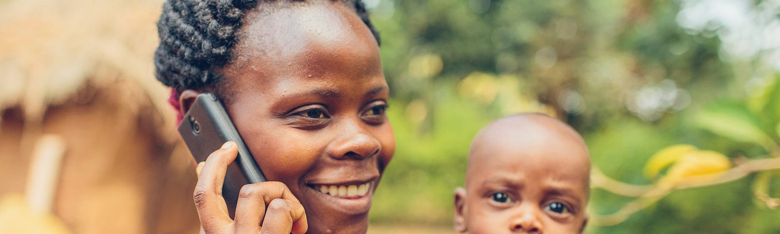 A smiling woman holds a mobile phone to her ear while also holding a small child in her other arm.