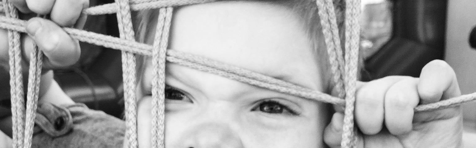 Angry young boy screaming and pushing face up through rope netting