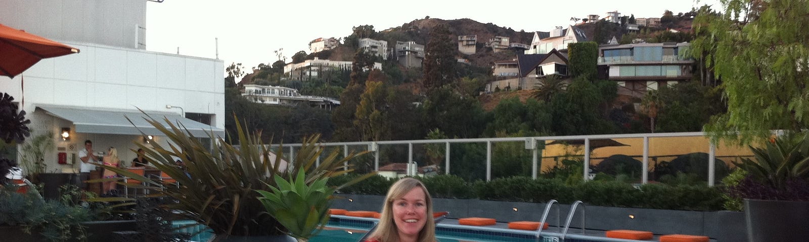 The author holding a beer sitting on a hotel rooftop terrace in LA with a pool in the background.