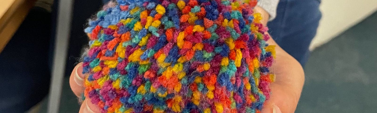 A hand holding a multicoloured pom-pom