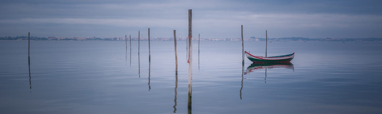 Still waters. No waves. Some sticks standing in the water. One boot. Image in blue grey tune. Stillness is our home.