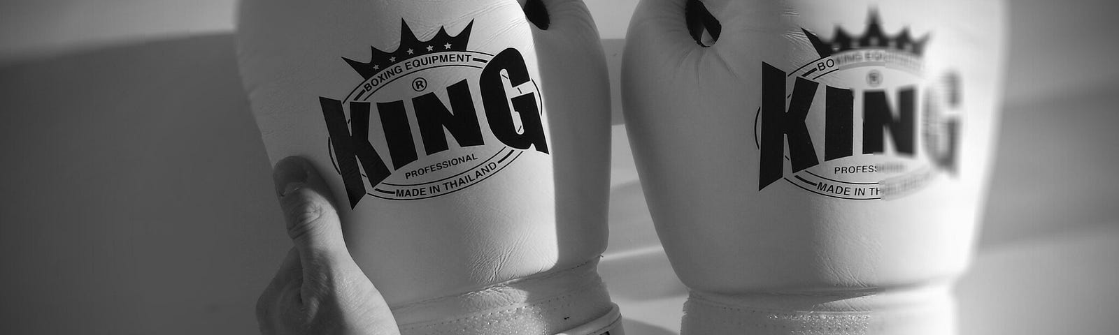 A pair of white King brand boxing gloves held by a hand, shown in black and white.