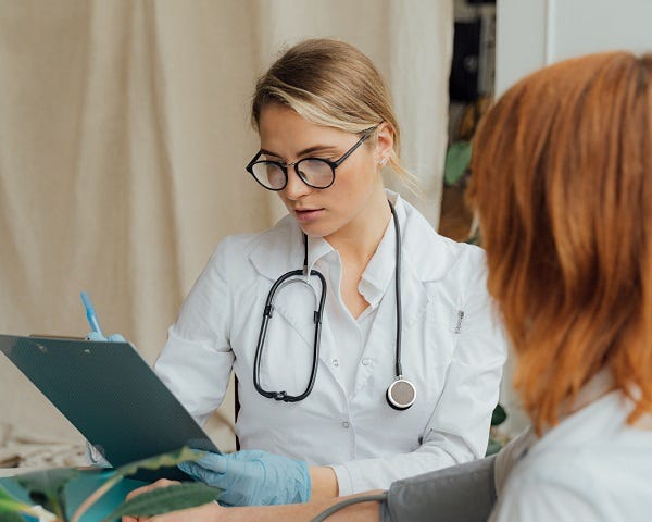 A patient is having a consultation with a female doctor. The doctor is wearing a traditional while doctor clothes with a stethoscope hanging on her neck.