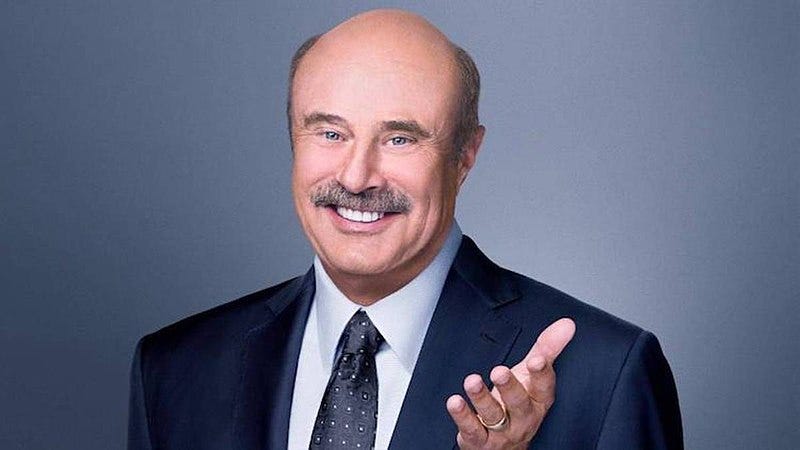 A professional profile photograph of Dr. Phil in a blue suit and tie, and crisp white shirt. He is posing with a smile and his hand is held out with his palm opened upward as a friendly looking gesture.