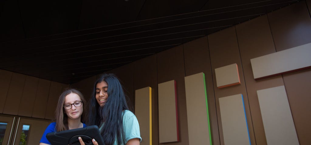 Photo of two students looking at a tablet in front of an MIT sign.