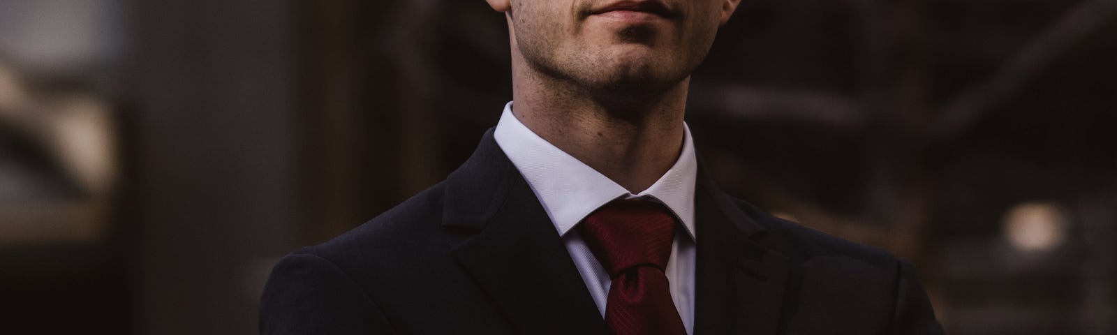 Man wearing suit with arms crossed and watch displayed.