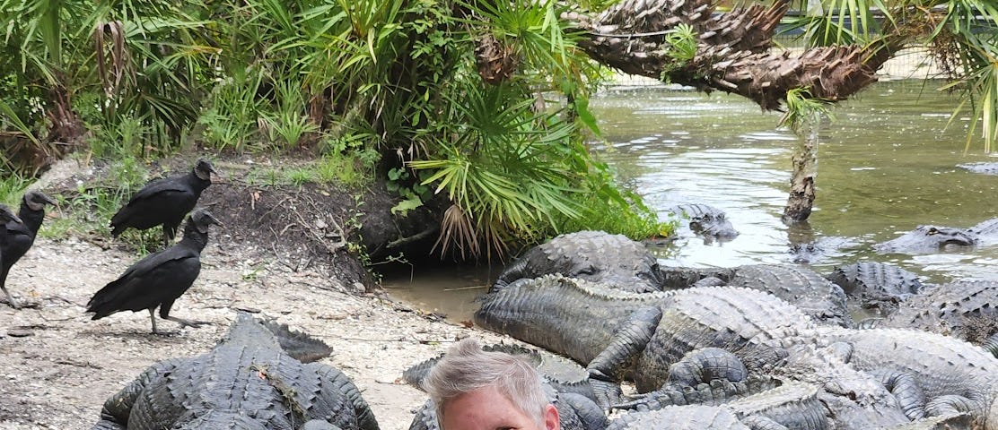 A ten-year-boy with his mom (the author) in front of many alligators with some big black birds nearby.