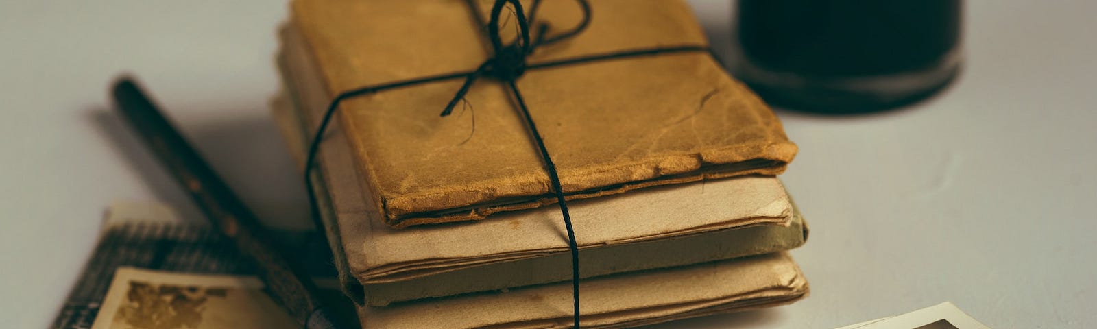 Stack of old letters tied in a bundle by a caligraphy pen and sepia-tone photos. Photo by Joanna Kosinska, Unsplash.