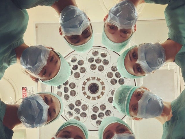 Medical personnel in scrubs with masks look down in a circle