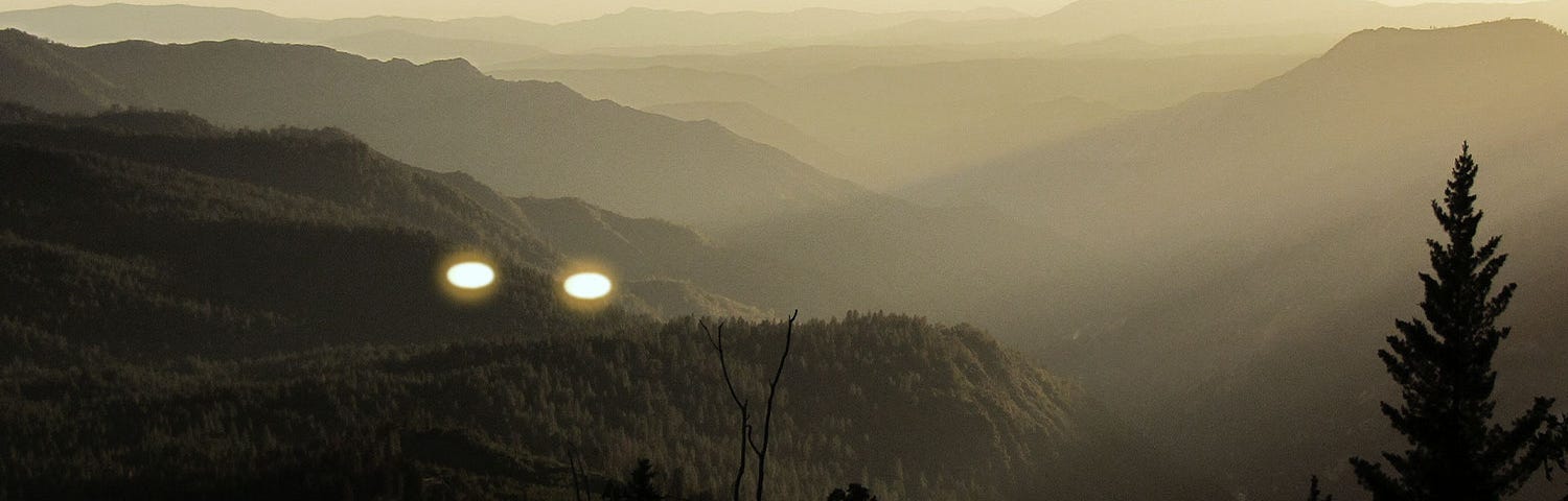 Two glowing objects hovering over a mountainous landscape.