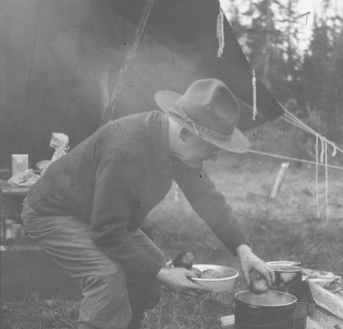 George Eastman cooking potatoes over a campfire