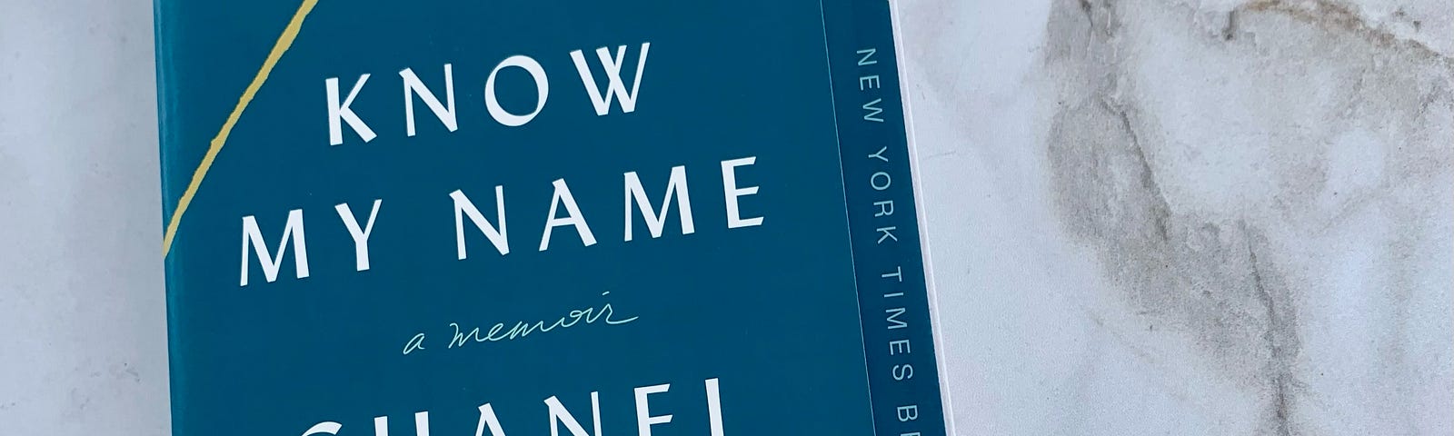 The author’s copy of Know My Name by Chanel Miller sitting on top of a marble countertop. The paperback cover is blue with golden lines. The book has a “NY Times Bestseller” sicker on it.