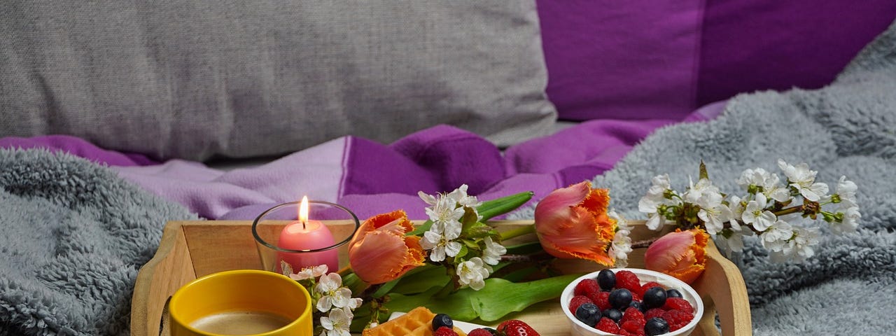 A breakfast tray full of food, sitting on a bed with purple covers.