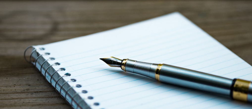 picture of a spiral bound notebook with a fountain pen laying on top