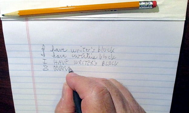 Hand with pencil and pad writing “I have writer’s block” over and over