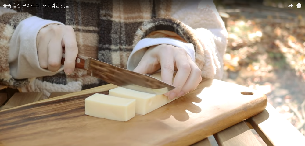 A woman slices butter on a wooden table outside in the forest.