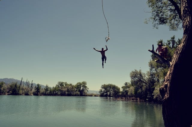 Man jumping from on high into a body of water, letting go of a rope