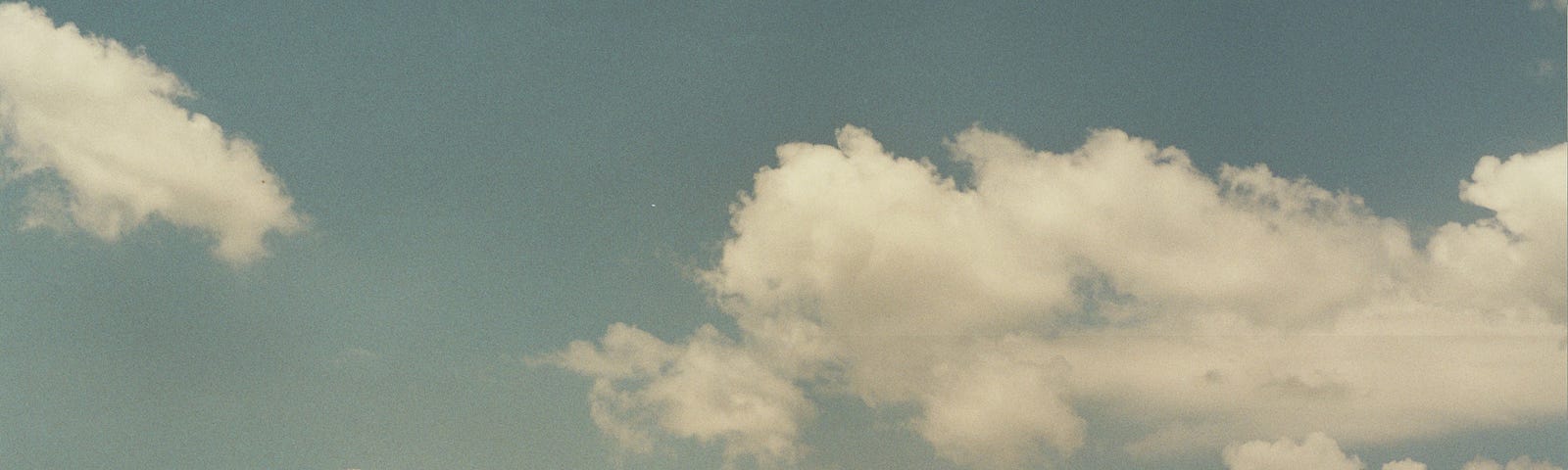 A hazy film photograph of a cloudy blue sky.