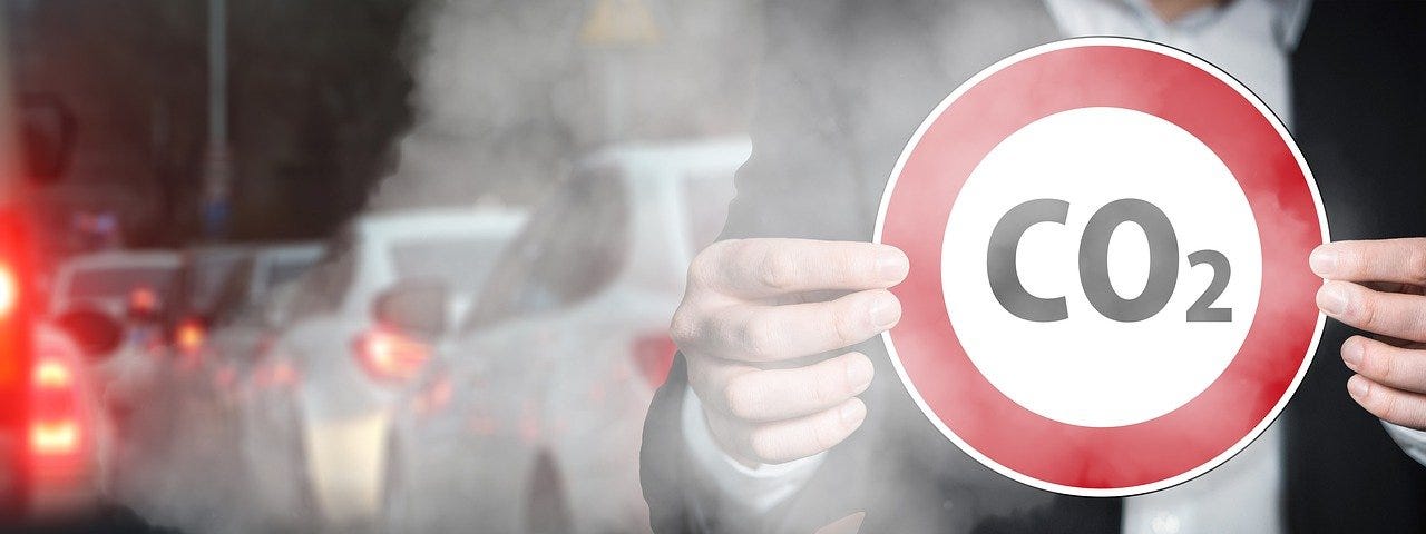 IMAGE: A row of cars emitting fumes and a person holding a traffic sign that says CO2