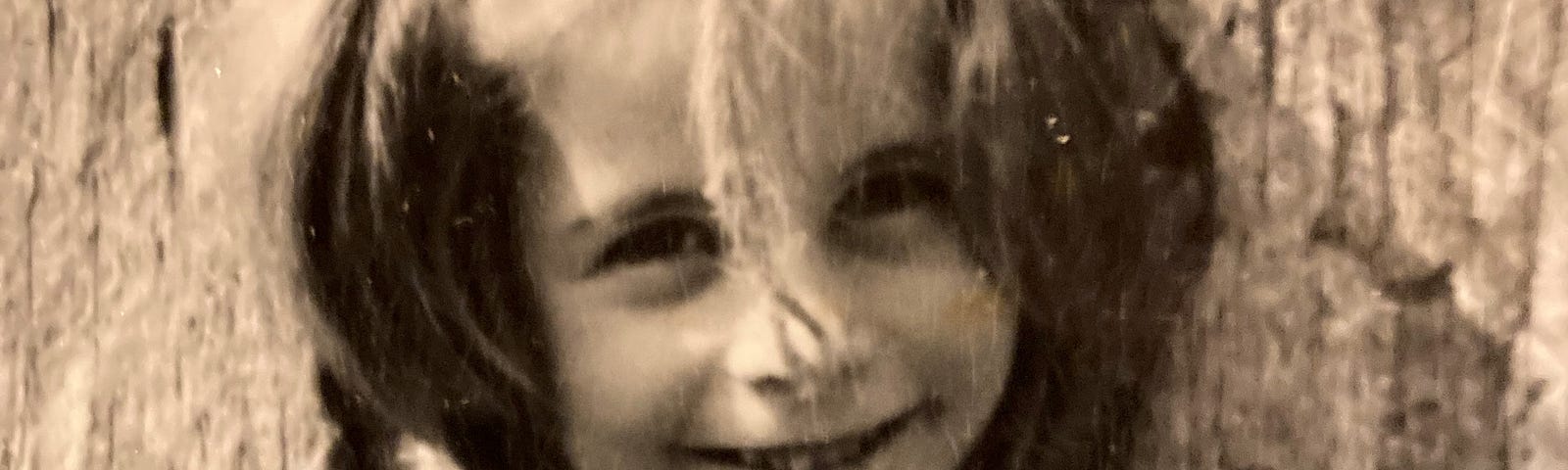 A young girl in an aged photograph sticks her head out between two pieces of wood