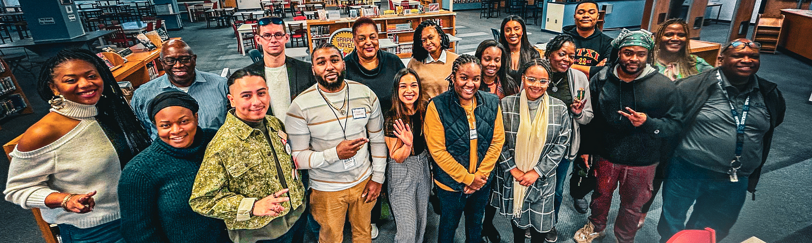 Group photo of SJIEP reporting fellowship participants at their 2024 kickoff event. The diverse team is smiling broadly, standing in a library with bookshelves in the background. They are informally arrayed in two rows, with some seated, showing a mix of casual and business attire, reflecting a vibrant and collaborative atmosphere.