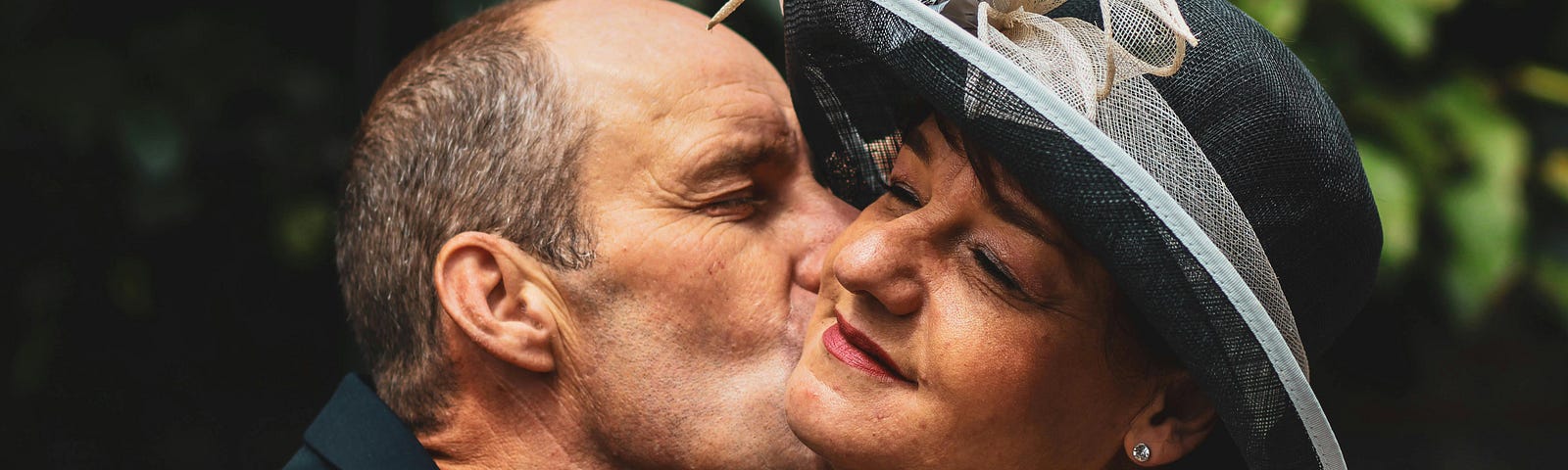 Photo of a man kissing a woman who’s wearing a hat and has her eyes closed.