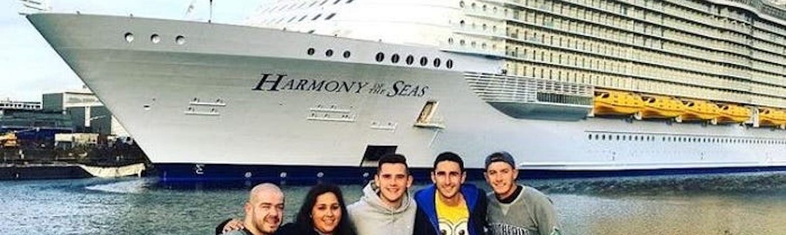 A group of people take a photo while standing in front of a cruise ship.