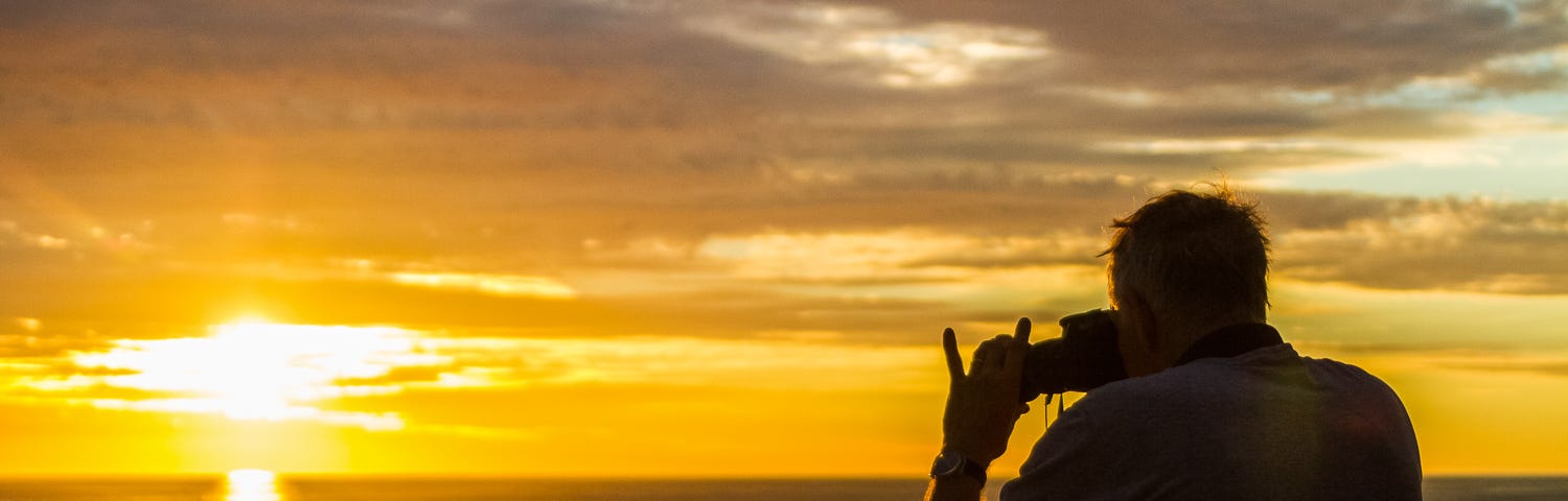 Man taking a photo with his camera. A beuatiful sunset in background.