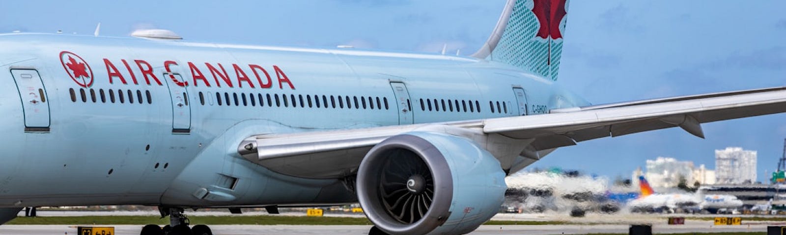 A plane painted in light blue with the red “Air Canada” lettering on the side is parked at an airport tarmac.