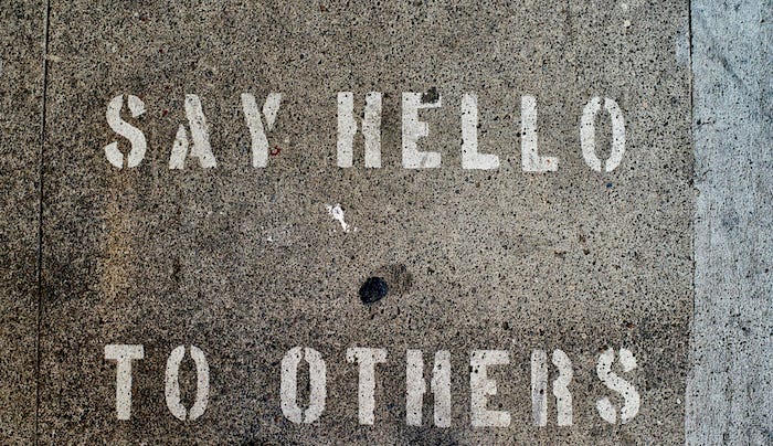 Bird’s eye view of the words “Say Hello to Others” spray-painted on a concrete sidewalk