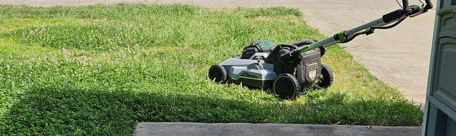 photo of lawn mower on patch of lawn next to driveway