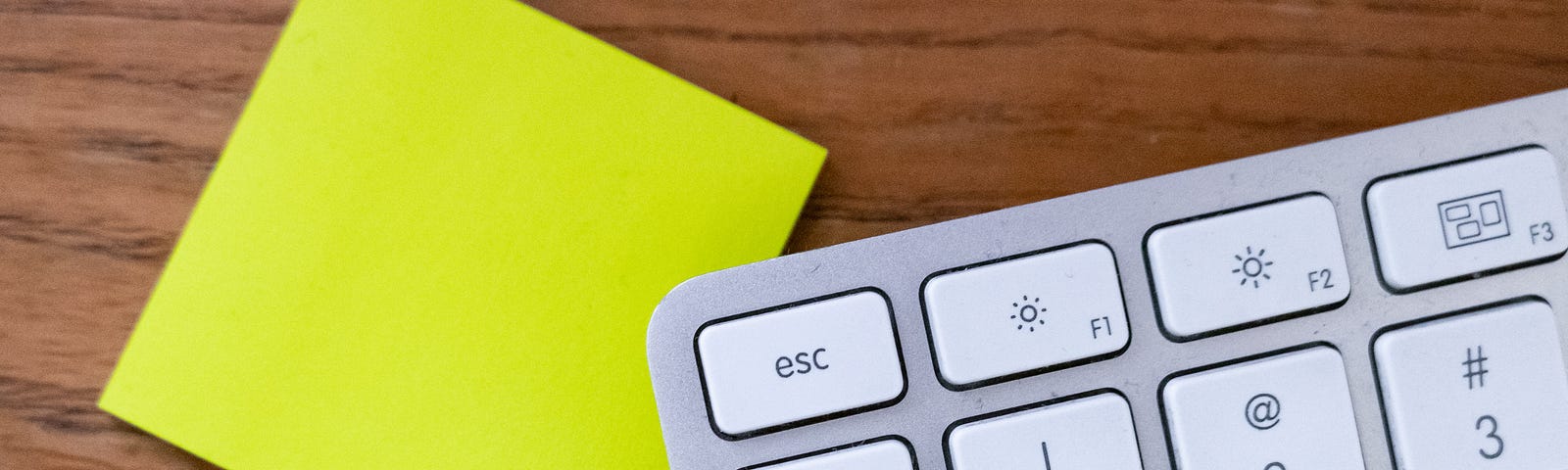 Photo of a computer keyboard with the tab and escape buttons in focus. The keyboard is overlapping a blank post-it note.