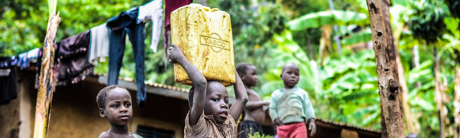 Copii din Africa într-un cartier sărac. Unul cară o canistră pe cap.