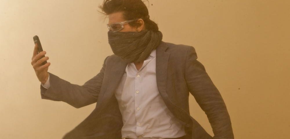 Tom Cruise as Ethan Hunt looking at his phone in a sandstorm.