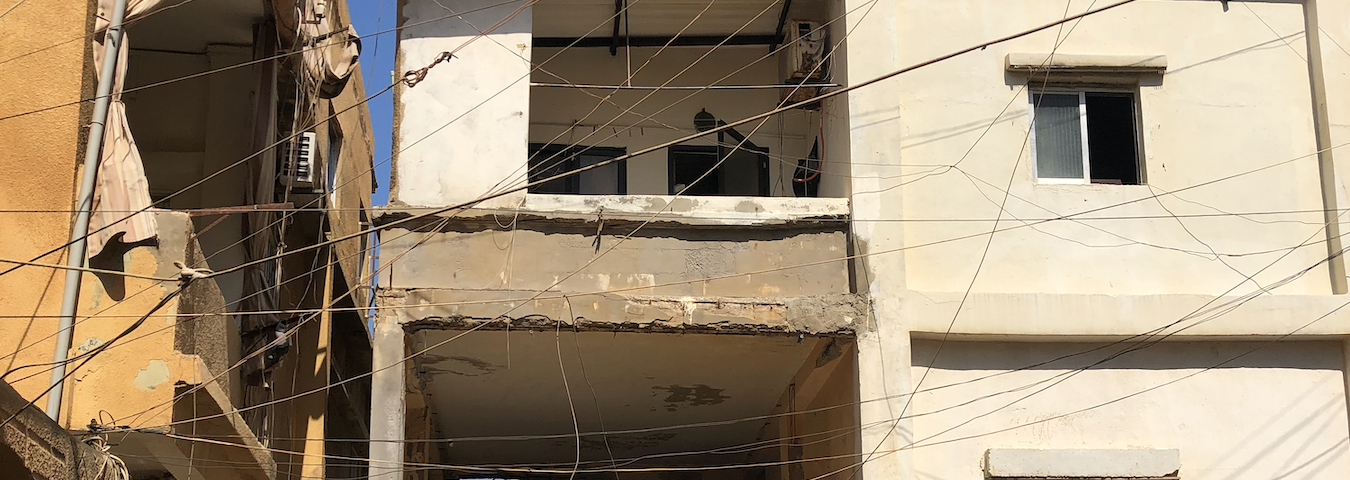 A woman in a headscarf walks past a dilapidated building.