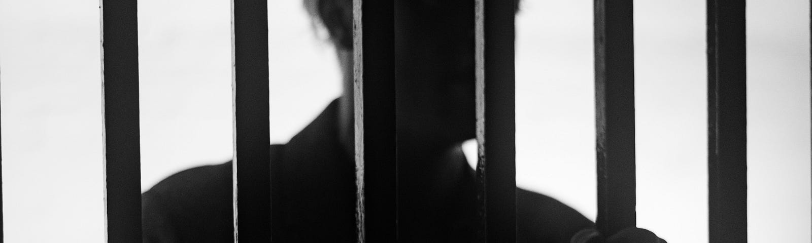 Silhouette of a man in a jail cell, clutching the bars