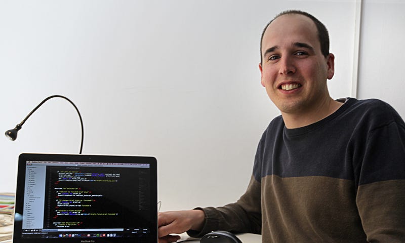 Homme à côté d’un ordinateur dans lequel on voit des lignes de code