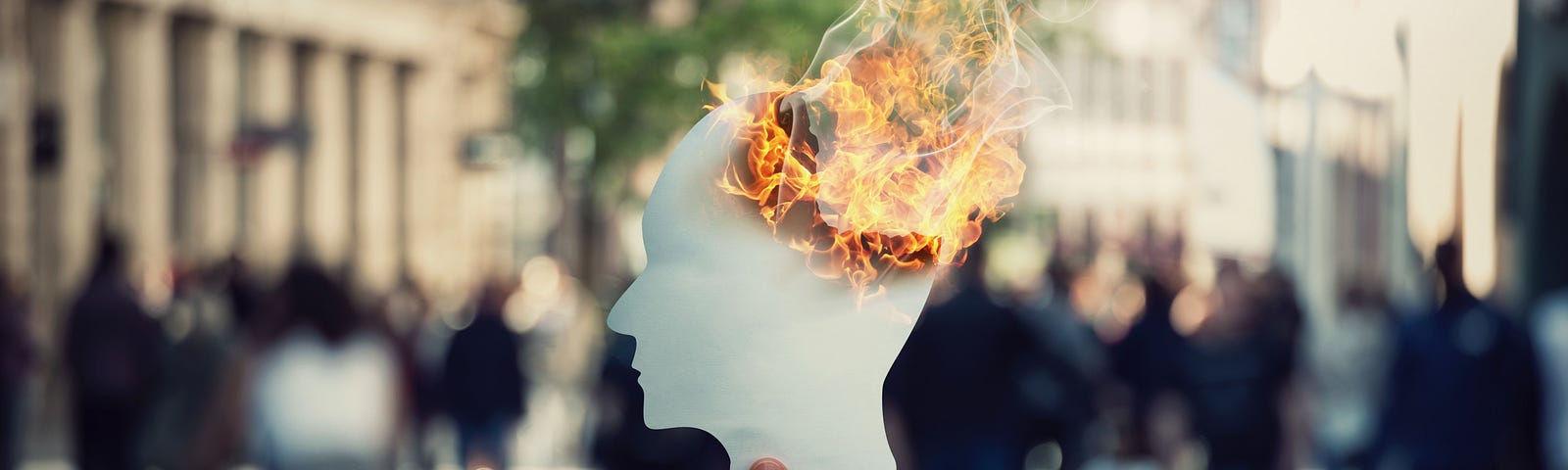 Burnout and stress concept as person hand holds a burning, human head shaped, paper sheet on a crowded street.