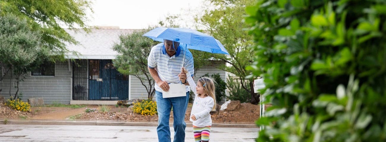 A man and young girl walk with an umbrella.