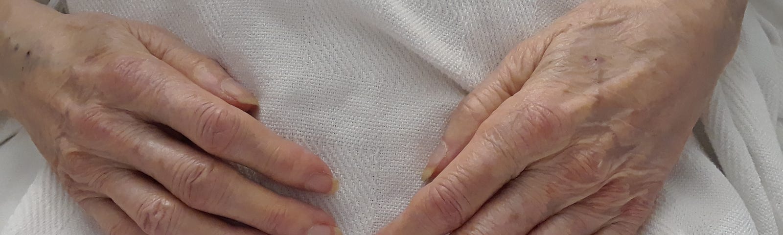 hands of an older woman, on her own stomach and lap.