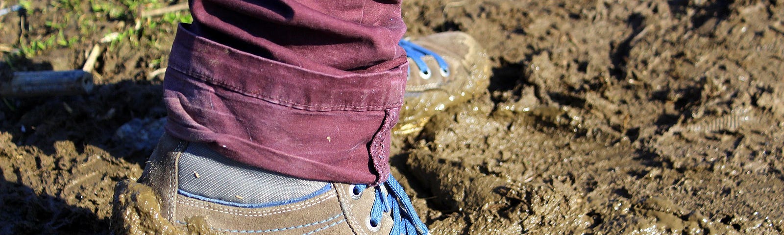 Photo of a pair of feet in walking shoes on a mud-sodden path