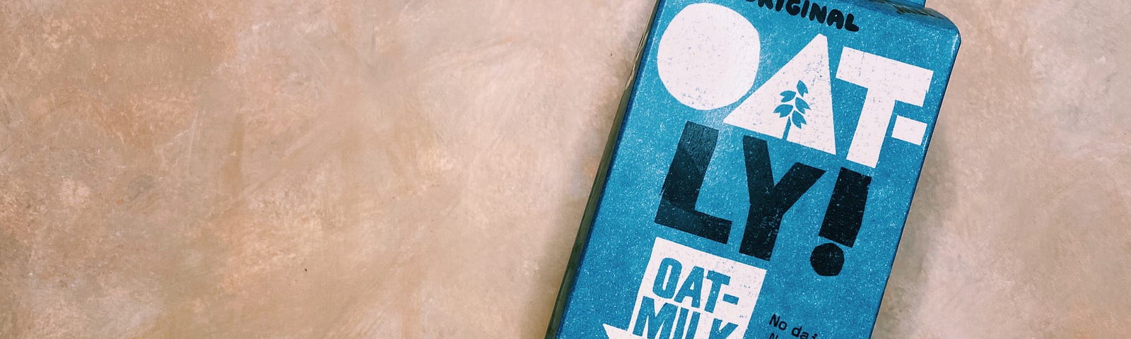 My Oatly milk from my fridge photographed with a painted peach background