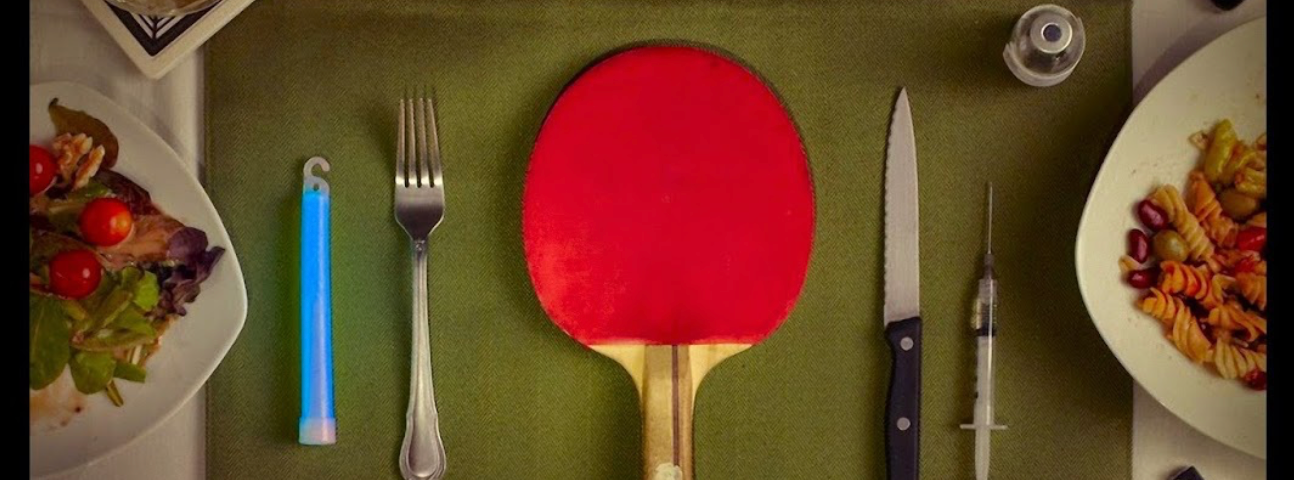 A picture of the film Coherence’s film poster. It shows a ping pong paddle, a fork, a knife, a blue glowstick, and a syringe on a dinner table