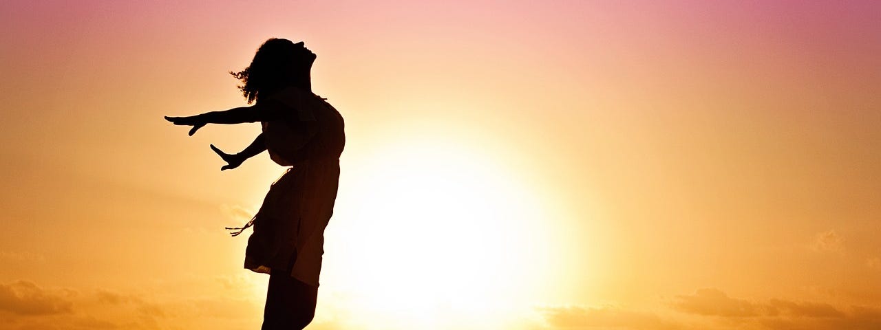 woman with arms out like flying silhouette at sunrise