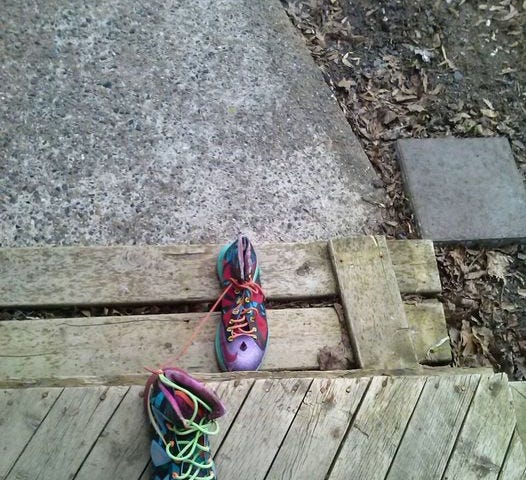 A pair of wildly painted, size 13 sneakers, all by themselves on a front porch step.